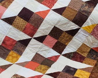 Pode incluir: Uma colcha com um design de patchwork que apresenta uma variedade de tecidos marrons, laranjas e amarelos. A colcha é feita de quadrados e triângulos, e os padrões dos tecidos são florais, geométricos e abstratos.