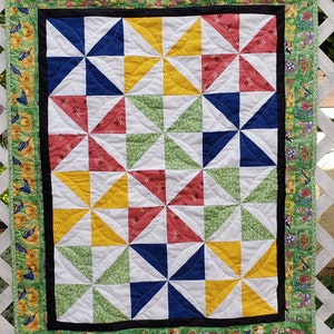 May include: A quilt with a windmill pattern in shades of red, yellow, green, blue, and white. The quilt is bordered with a floral print fabric.