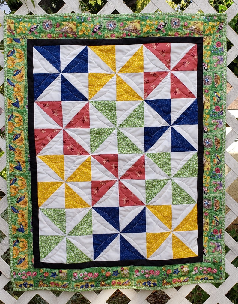 May include: A quilt with a windmill pattern in shades of red, yellow, green, blue, and white. The quilt is bordered with a floral print fabric.