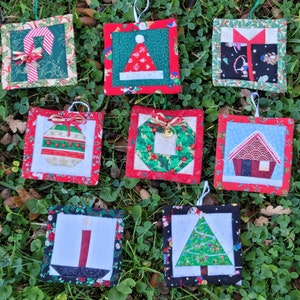 May include: Nine handmade Christmas ornaments with various holiday themes. The ornaments are square and feature a variety of designs, including a candy cane, a Santa hat, a gift box, an ornament, a wreath, a gingerbread house, a candle, and a Christmas tree. The ornaments are all made with fabric and are decorated with various embellishments.
