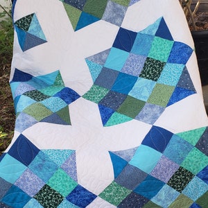 May include: A white quilt with a blue and green patchwork design. The quilt is made up of squares and triangles, and the colours are arranged in a geometric pattern.