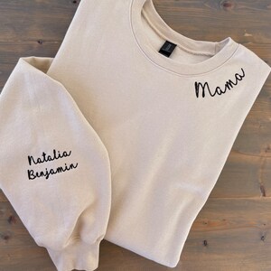 May include: A beige sweatshirt with the word "Mama" embroidered on the right shoulder and the names "Natalia" and "Benjamin" embroidered on the left sleeve.