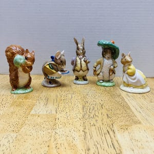 May include: A collection of five ceramic figurines featuring woodland creatures. The figurines include a squirrel holding a green object, a mouse with a basket, a rabbit in a vest, a rabbit in a coat and hat, and a mouse in a yellow dress. Each figurine is approximately 3 inches tall.