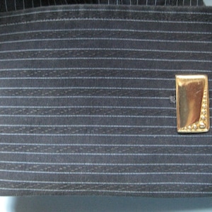 Puede incluir: Un par de gemelos de oro con un diseño texturizado. Los gemelos están sobre un fondo de tela gris oscuro a rayas.