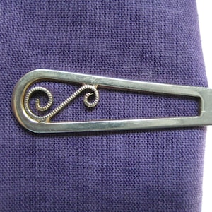 Puede incluir: Pinza de corbata de plata con un diseño decorativo de espiral.