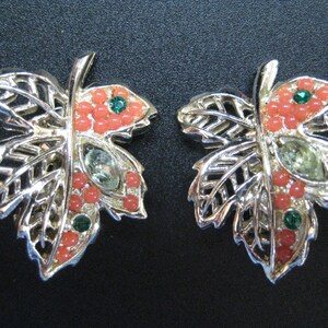 May include: A pair of silver tone earrings shaped like maple leaves with pink and green rhinestones.