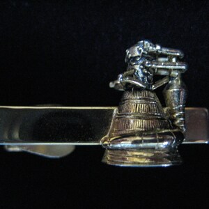 Pode incluir: Um prendedor de gravata dourado com um modelo detalhado de um foguete.