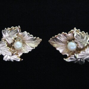 Peut inclure: Une paire de boucles d'oreilles en or avec un motif de feuilles et une seule perle au centre de chaque boucle d'oreille.