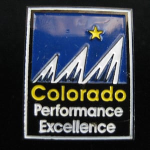 May include: A blue and white enamel pin with a yellow star and the text "Colorado Performance Excellence" in white letters on a black background.
