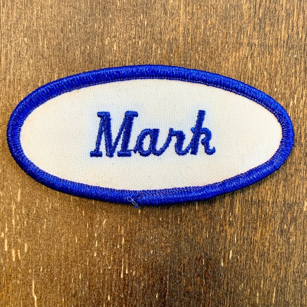 Mark. A white work shirt name patch that says "Mark" in blue script with blue border