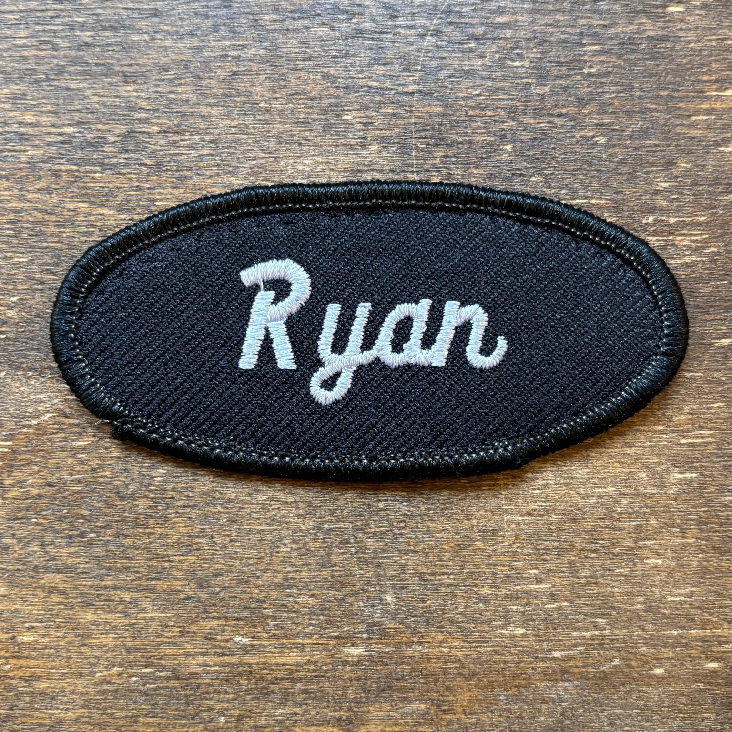 Ryan - A black work shirt patch that says "Ryan" in white script
