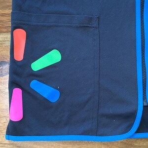 May include: A black vest with a blue zipper and a blue trim around the bottom. The vest has a large pocket on the left side and a Walmart logo on the front. The logo is made up of four colored shapes: red, green, blue, and pink.