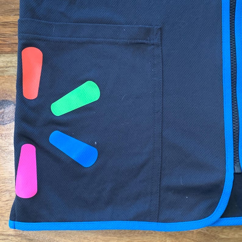 May include: A black vest with a blue zipper and a blue trim around the bottom. The vest has a large pocket on the left side and a Walmart logo on the front. The logo is made up of four colored shapes: red, green, blue, and pink.
