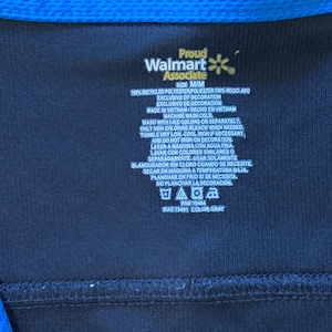 May include: A black Walmart Associate uniform tag with blue trim. The tag has white text that reads 'Proud Walmart Associate', 'Size M/M', '100% Recycled Polyester/Poliéster 100% Reciclado', 'Exclusive of Decoration', 'Exclusivo de Decoración', 'Made in Vietnam/Hecho en Vietnam', 'Machine Wash Cold', 'Wash with like colors or separately', 'Only non chlorine bleach when needed', 'Tumble dry low. Cool iron if necessary, and do not iron on decoration', 'Lavar a máquina con agua fría', 'Lavar con colores similares o separadamente', 'Usar solamente blanqueador sin cloro cuando se necesite', 'Secar en máquina a temperatura baja', 'Planchar en frío si se necesita, no planchar la decoración', 'RN 19484', 'SUG 75491 COLOR GRAY'. The tag also has several care instructions symbols.