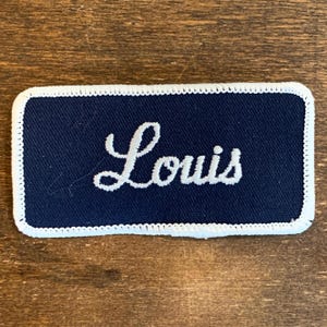 Louis. A blue work shirt patch that says "Louis" in white script with white border