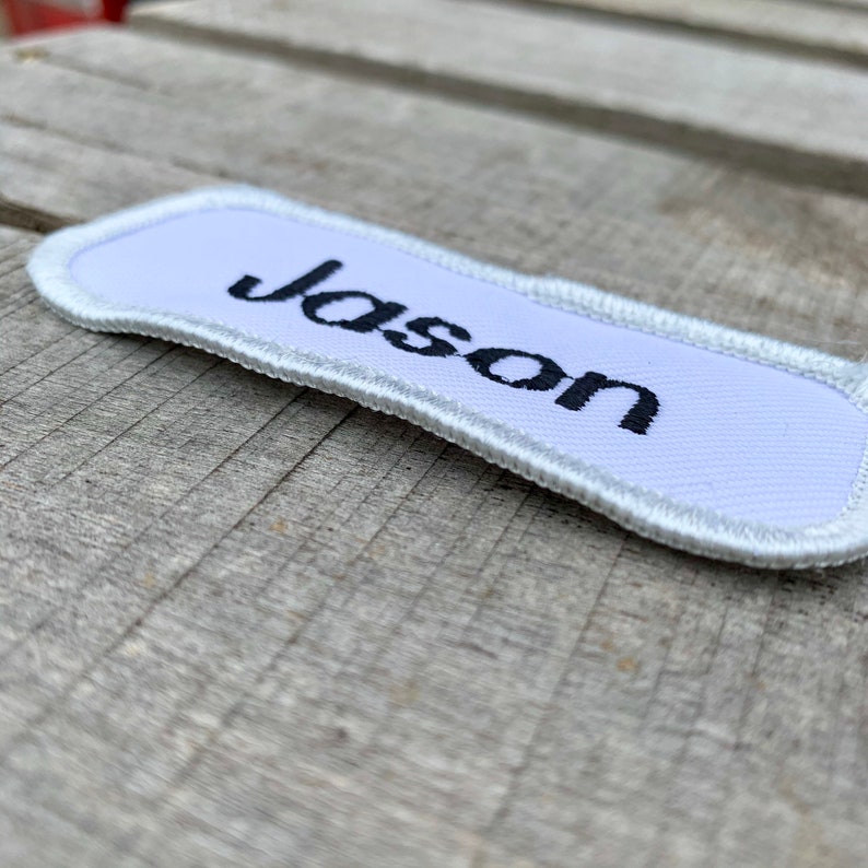 A white work shirt name patch that says Jason in print script Jason