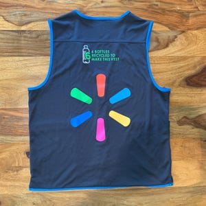 May include: A black sleeveless vest with a blue trim. The vest has a large multi-colored starburst logo on the back. The text '6 bottles recycled to make this vest' is printed above the logo.