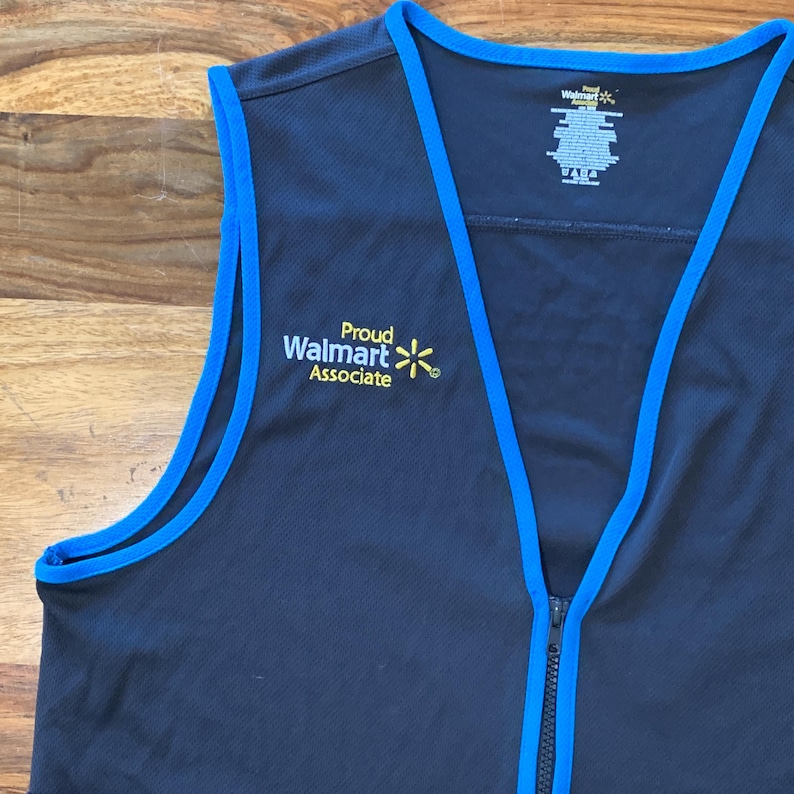 May include: A black vest with blue trim and a zipper. The vest has the text 'Proud Walmart Associate' and a yellow Walmart star logo embroidered on the front.
