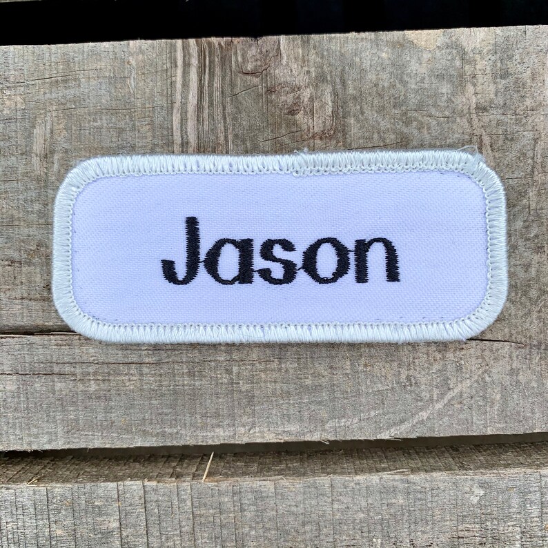 A white work shirt name patch that says Jason in print script Jason