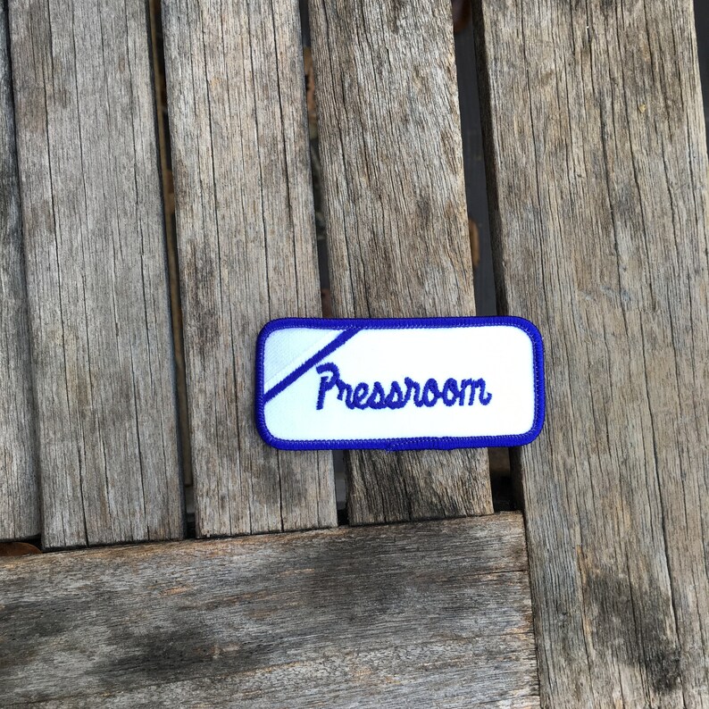 Pressroom A white work shirt uniform patch that says Pressroom in blue script with blue border.