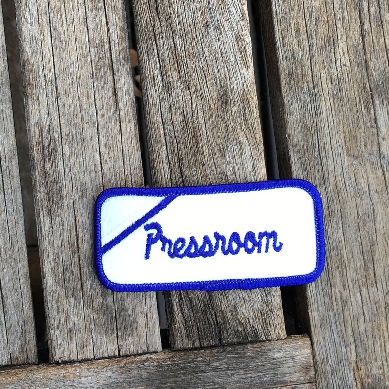 Pressroom A white work shirt uniform patch that says Pressroom in blue script with blue border.