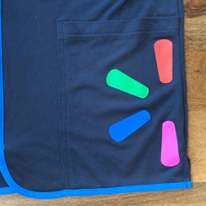 May include: A black work uniform with a blue trim and a blue, green, pink, and red Walmart logo on the pocket.