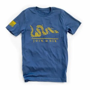 K&ouml;nnte beinhalten: Marineblaues T-Shirt mit gelber Grafik einer segmentierten Schlange und dem Schriftzug "JOIN, or DIE." Auf dem linken &Auml;rmel befindet sich ein gelbes Flaggen-Design. Das Shirt ist aus weichem Material und f&uuml;r den Alltag geeignet.