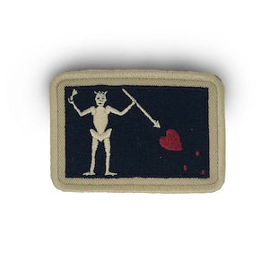 May include: A beige embroidered patch with a black background featuring a white skeleton holding a spear and a red heart. The skeleton is wearing a crown.