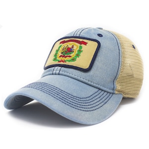 May include: A light blue baseball cap with a tan mesh back and a rectangular patch on the front. The patch features the West Virginia state seal, including a red ribbon, green foliage, and a central illustration, all bordered in dark blue.