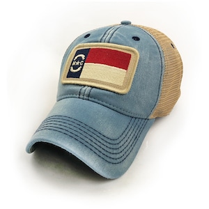 Trucker hat with khaki colored mesh backing, faded blue cotton front panel and bill with tan stitching. Ballcap has an embroidered patch of the North Carolina flag in in the center.