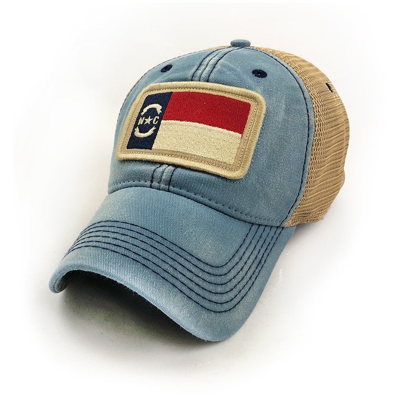 Trucker hat with khaki colored mesh backing, faded blue cotton front panel and bill with tan stitching. Ballcap has an embroidered patch of the North Carolina flag in in the center.