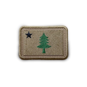 May include: A tan embroidered patch with a green pine tree and a black star on a tan background.