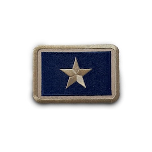 May include: A beige embroidered patch with a dark blue background and a gold star in the center.