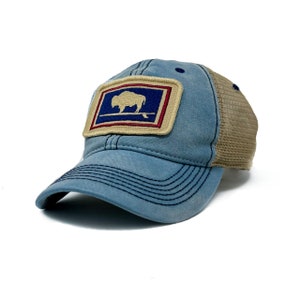 May include: A blue baseball cap with a mesh back and a patch featuring a white bison on a blue background, framed by red and tan. The cap has a curved brim and black stitching.