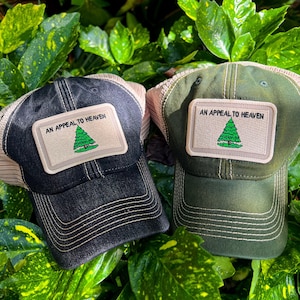 May include: Two black and green trucker hats with a beige mesh back. Each hat has a beige patch with the text "An Appeal to Heaven" and a green stylized tree.