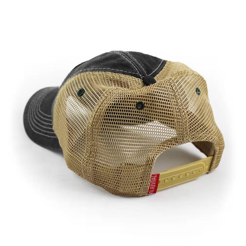 May include: A black and tan trucker hat with a mesh back. The hat has a curved brim and a snapback closure. The brim and top of the hat are black, while the back is tan mesh. A red tag with white text is attached to the adjustable strap.