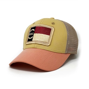 May include: A yellow and peach trucker hat with a patch of the South Carolina state flag on the front.