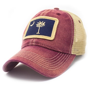 May include: A burgundy and beige trucker hat with a patch featuring the South Carolina state flag. The flag is blue with a crescent moon and a palmetto tree.