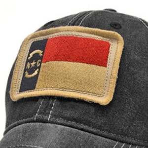 May include: A black baseball cap with a vintage-style North Carolina state flag patch on the front. The patch features the state's flag colors of red, white, and gold.