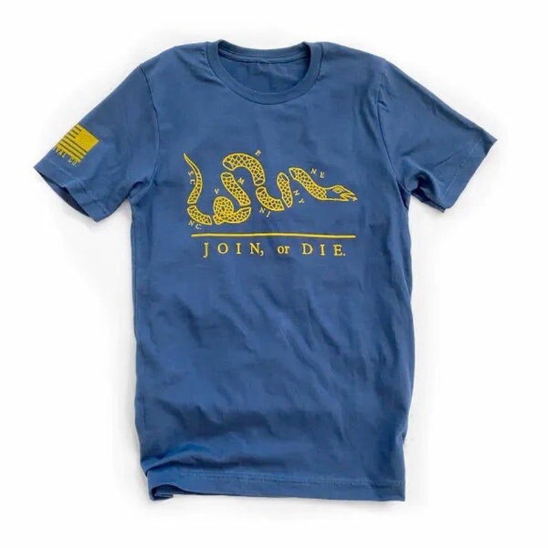 K&ouml;nnte beinhalten: Marineblaues T-Shirt mit gelber Grafik einer segmentierten Schlange und dem Schriftzug "JOIN, or DIE." Auf dem linken &Auml;rmel befindet sich ein gelbes Flaggen-Design. Das Shirt ist aus weichem Material und f&uuml;r den Alltag geeignet.