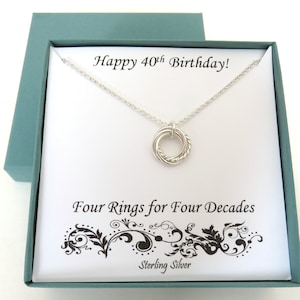 May include: A silver necklace with a four-ring pendant in a teal gift box. The box has a white card inside with the text "Happy 40th Birthday!" and "Four Rings for Four Decades Sterling Silver."