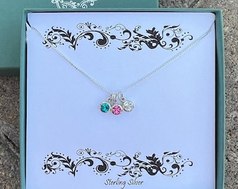 May include: A silver necklace with three small charms, each with a different coloured crystal: teal, pink, and clear. The necklace is displayed in a white box with the words "Sterling Silver" printed on the bottom.