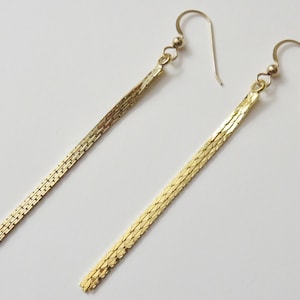 May include: A pair of long, gold, chain-link earrings. The earrings are made of a thin, delicate chain that hangs down from a small hook.