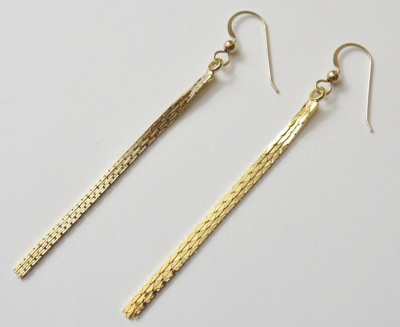 May include: A pair of long, gold, chain-link earrings. The earrings are made of a thin, delicate chain that hangs down from a small hook.