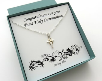 May include: A silver necklace with a white cross pendant and a gold accent. The necklace is in a teal box with a white card that reads "Congratulations on your First Holy Communion" and "Sterling Silver".