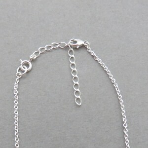 May include: A silver chain necklace with a lobster clasp closure and a small extension chain.
