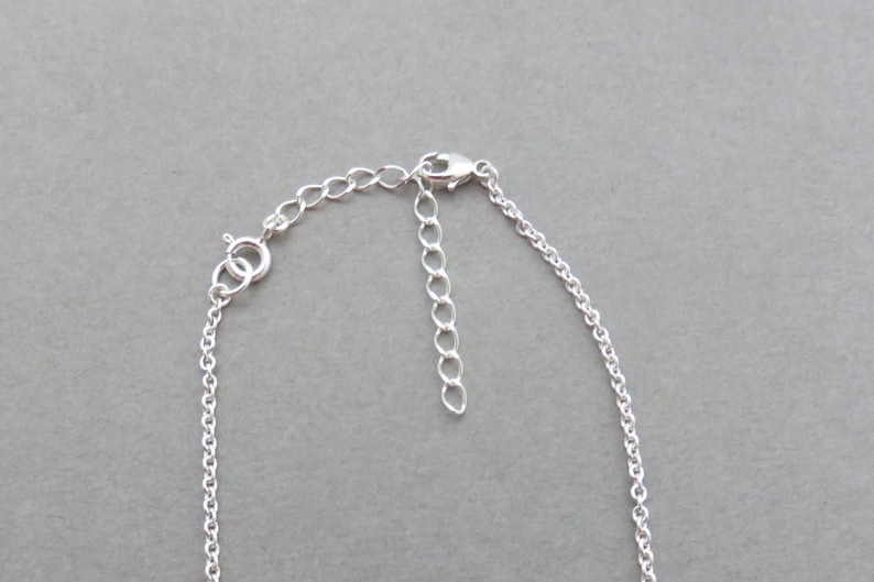 May include: A silver chain necklace with a lobster clasp closure and a small extension chain.