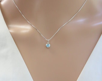 May include: A delicate silver chain necklace with a small, round, light blue gemstone pendant.