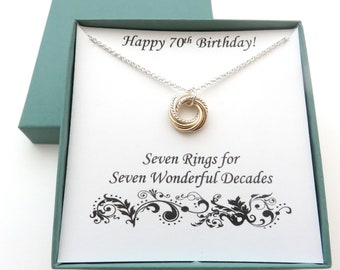 May include: A silver necklace with a gold and silver seven-ring pendant in a teal gift box. The card inside the box reads "Happy 70th Birthday!" and "Seven Rings for Seven Wonderful Decades."