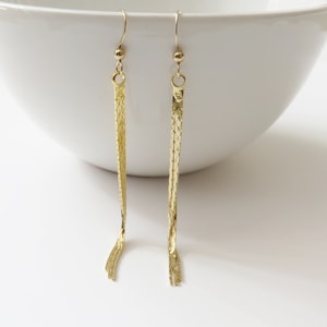 May include: A pair of gold-tone dangle earrings with a chain link design. The earrings are long and slender, and they have a simple, elegant look.